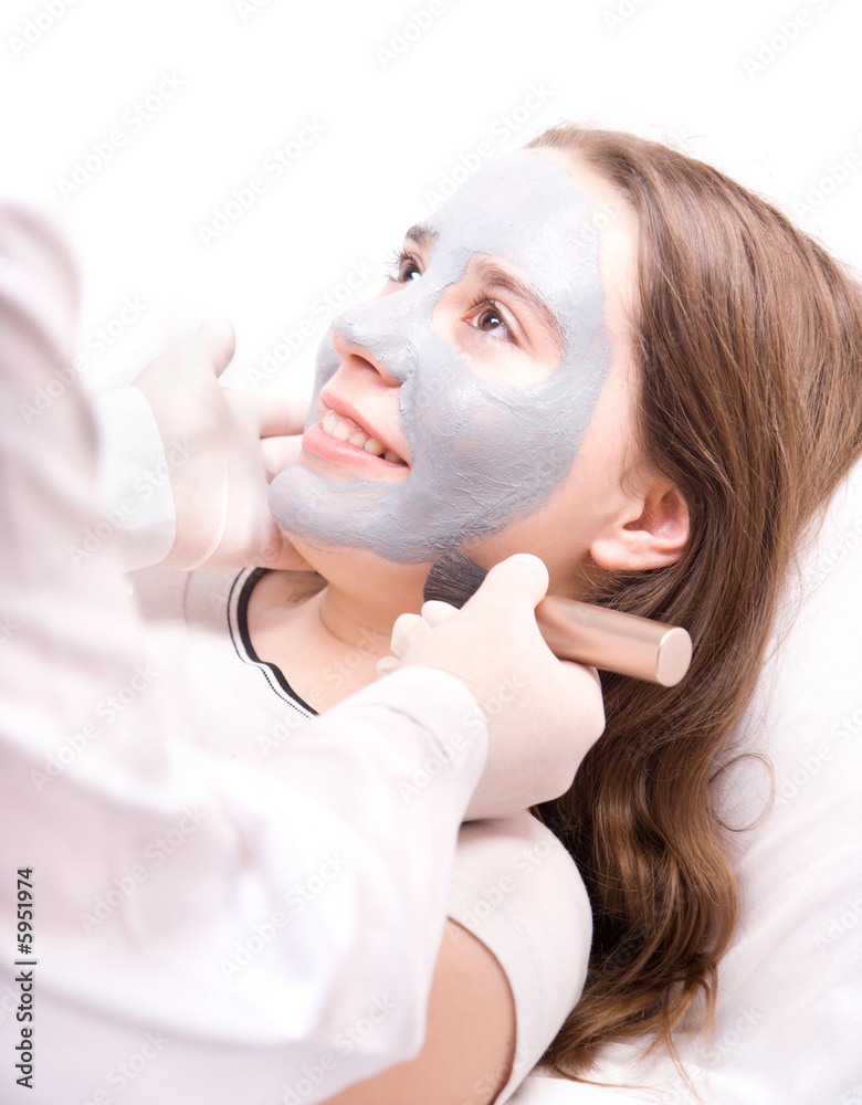 Beautician applying a clay mask on face young woman