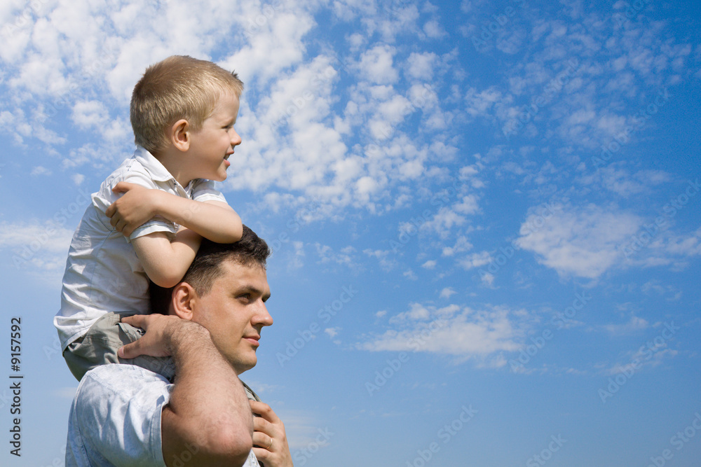 Little son sits on father`s shoulders outdoors