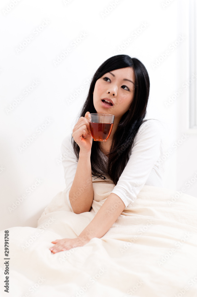 beautiful asian woman drinking tea on the bed