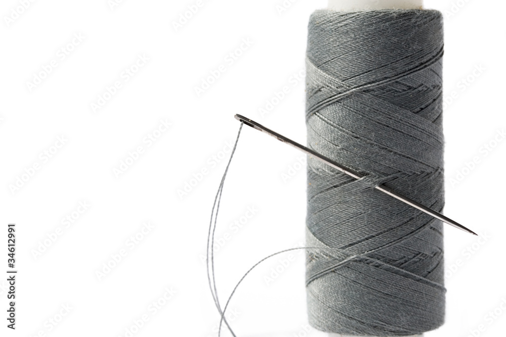 Thread bobbin and needle on white background