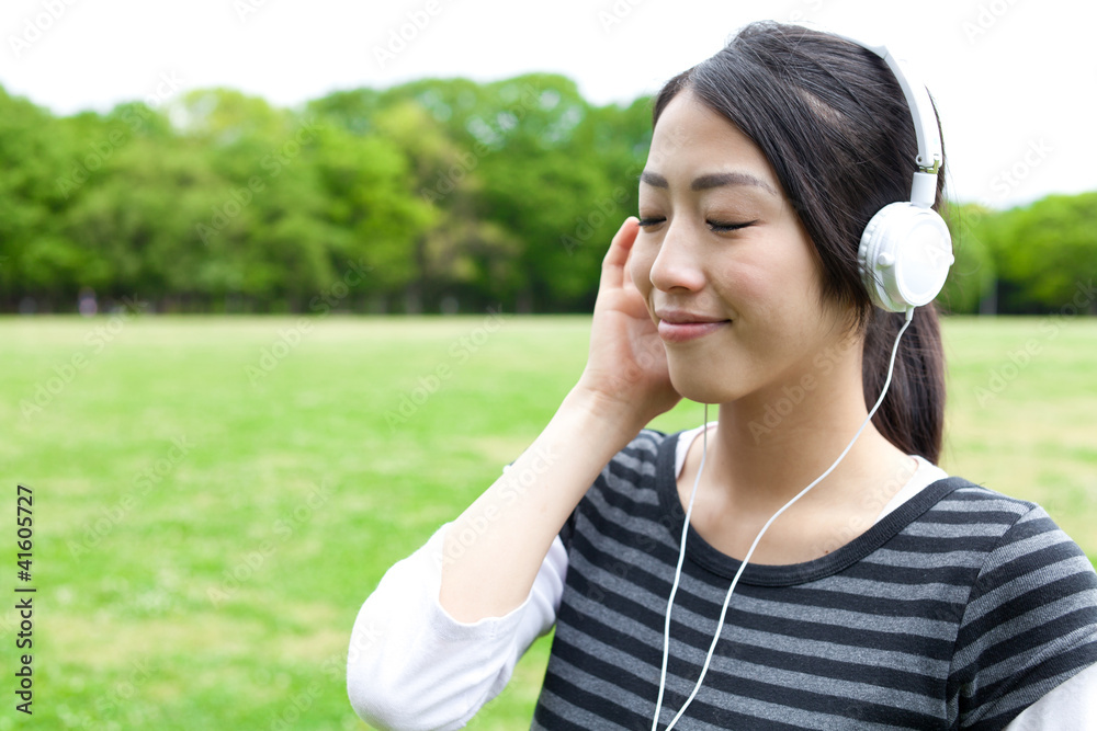 迷人的亚洲女人在公园里听音乐