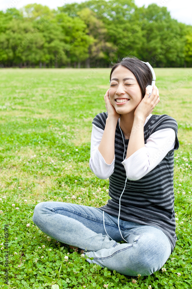 迷人的亚洲女人在公园里听音乐