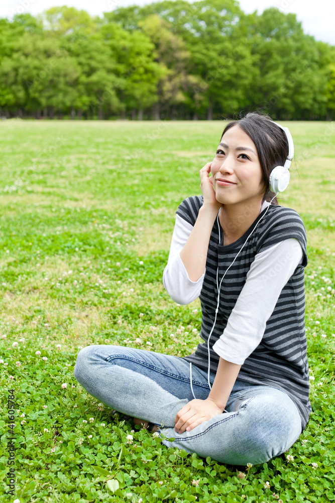 迷人的亚洲女人在公园里听音乐