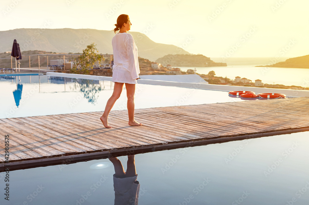 Woman walking at sunrise near swimming pool in Greece