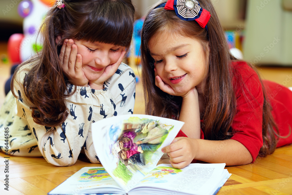 two beautiful little girls reading book at home