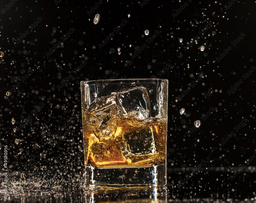 Whiskey splashing around glass, isolated on black background