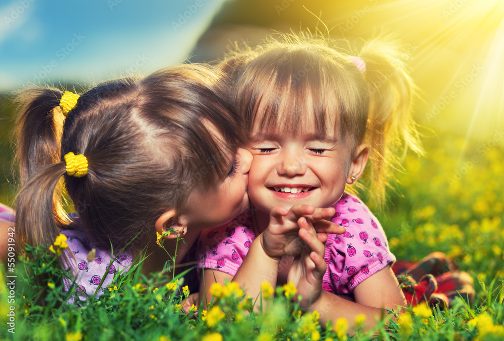 happy girls twin sisters kissing and laughing in the summer outd