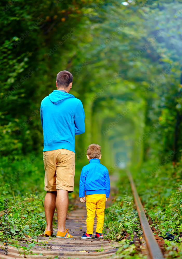 father and son walking on rails in green tonel