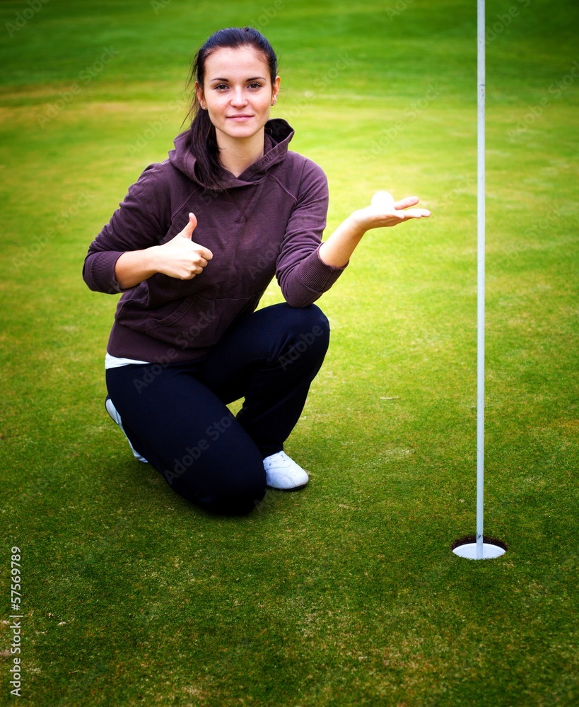 Young woman golf player holding ball giving Thumbs Up sign