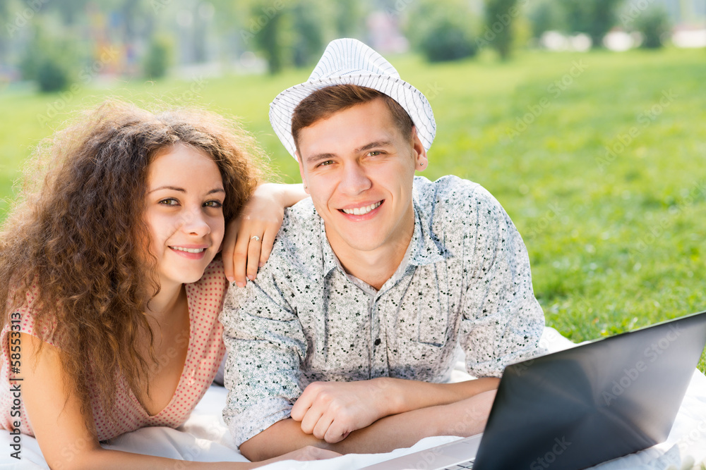 couple lying together in a park with laptop