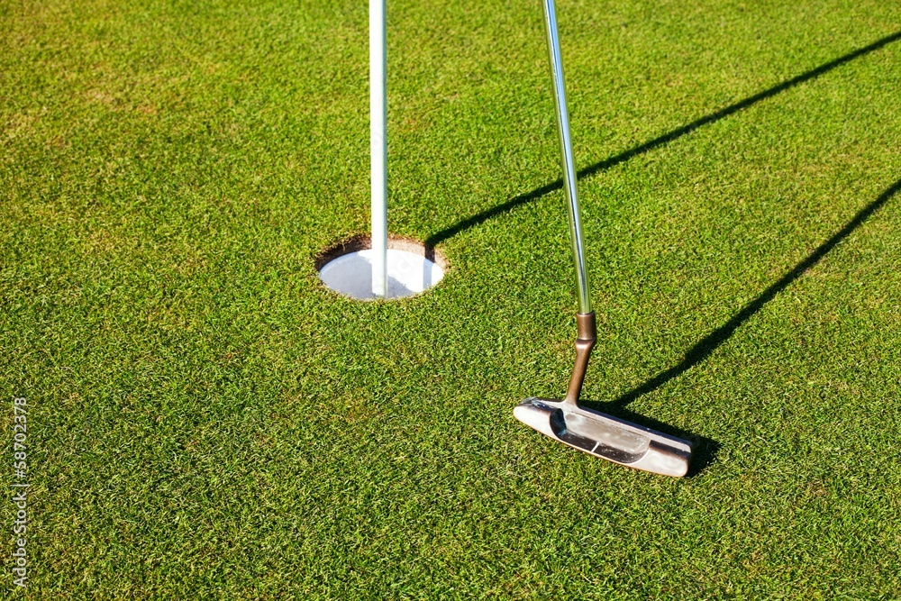 Golf club and cup on green, closeup