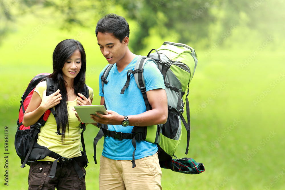 Happy couple going on a hike together looking at tablet pc in th