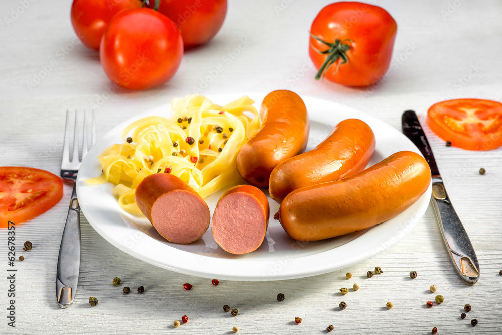 Sausages with pasta and tomatoes on a plate on white desk