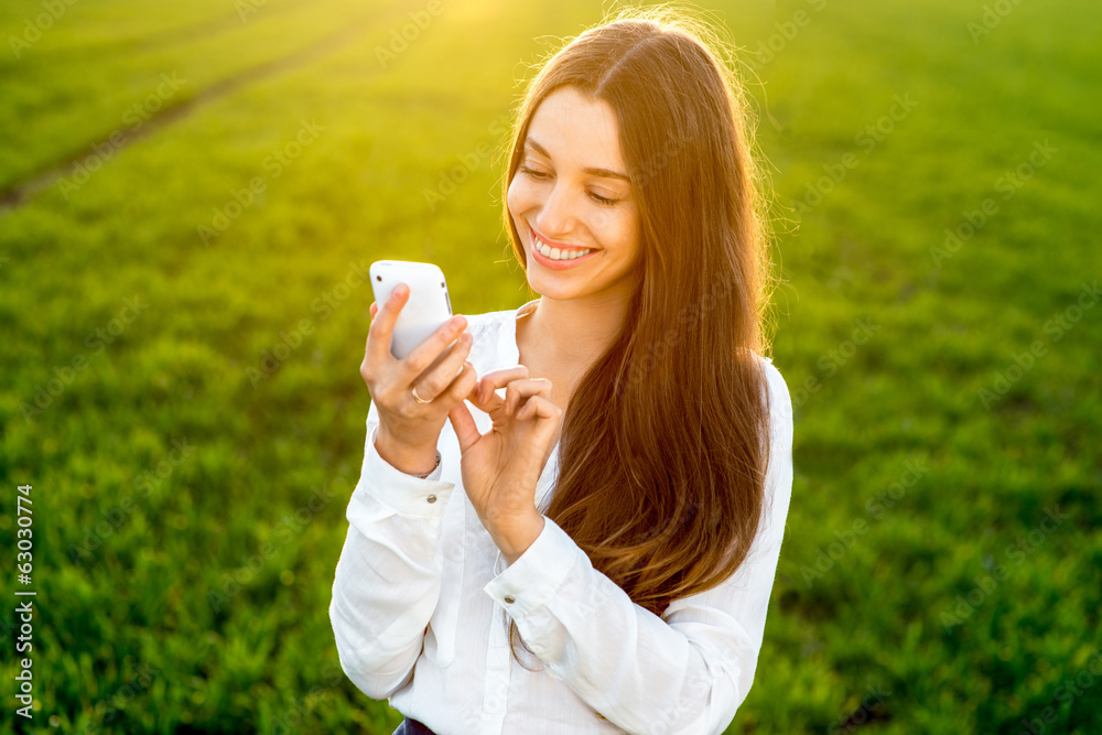 Young woman laughing and typing message in smart phone in the gr