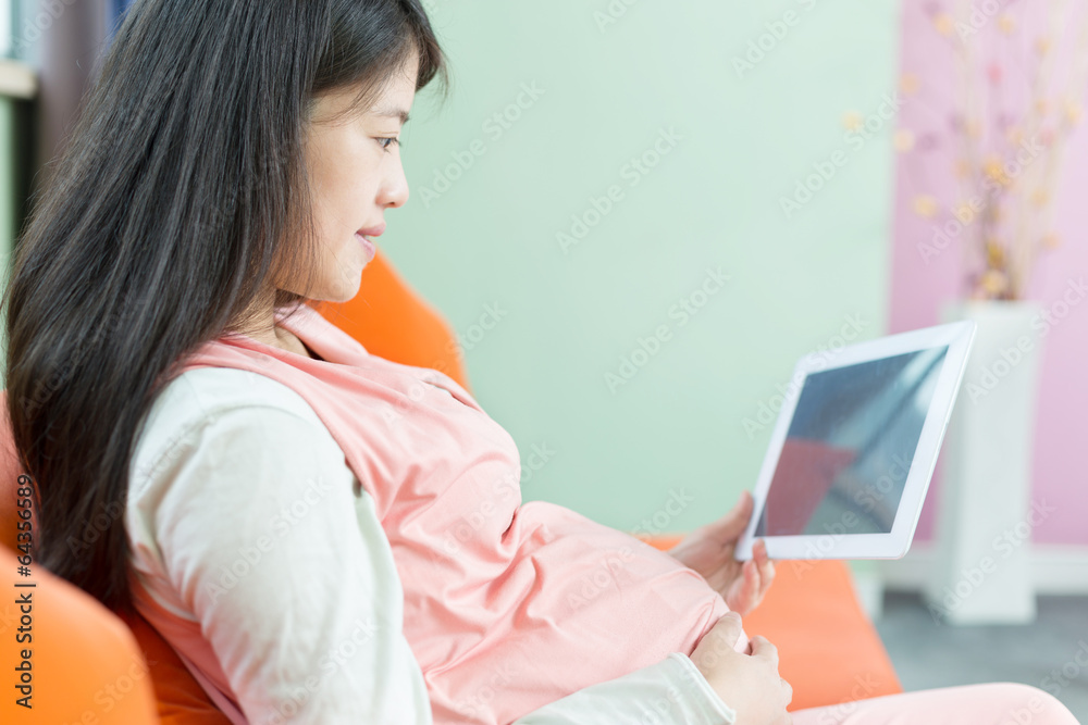 Happy pregnant woman looking at camera, using a digital tablet