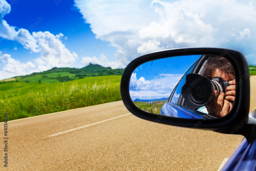 Photographer in car mirror drives near valley