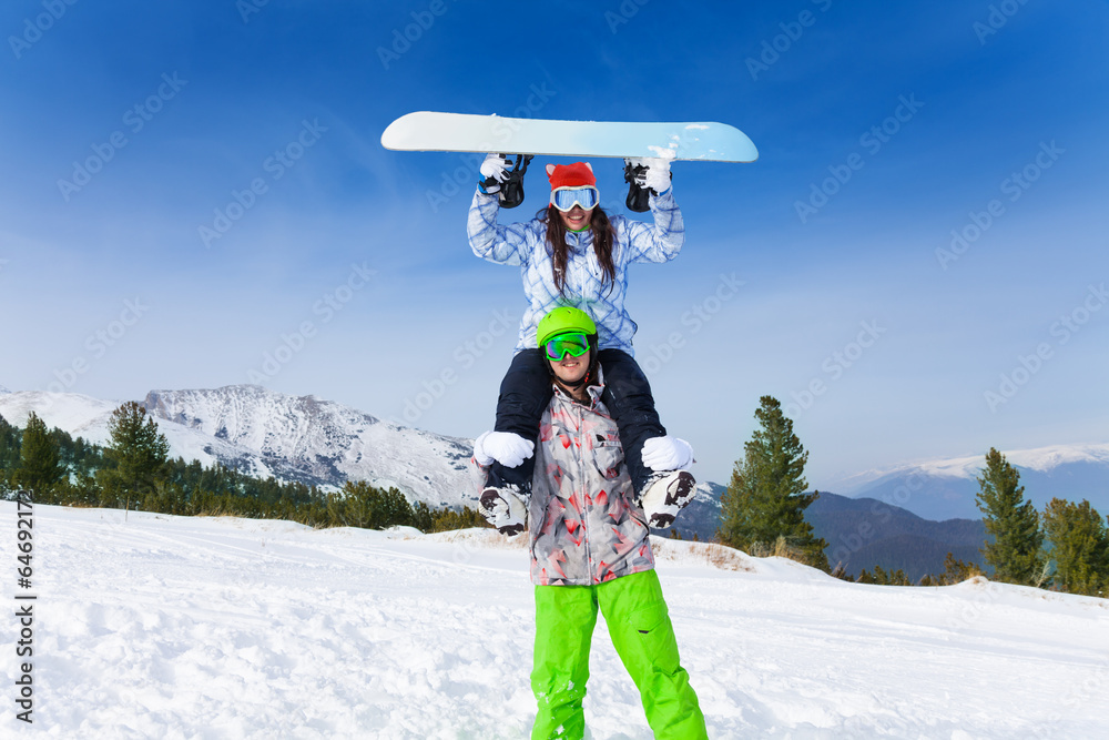 戴着滑雪面罩的男子抱着一个举着木板的女孩