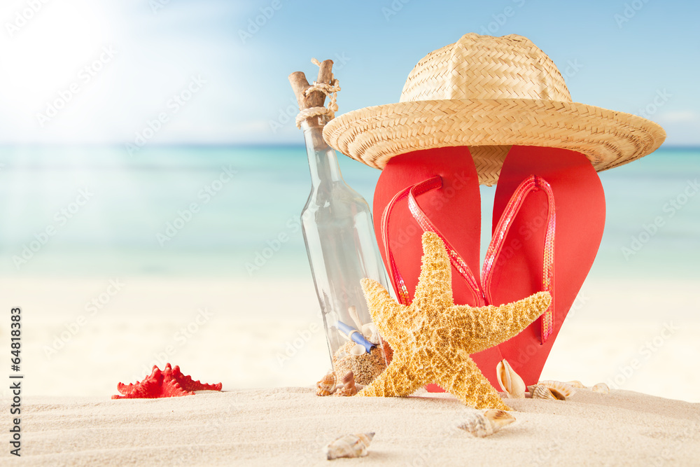 Summer beach with bottle, straw hat and sandals