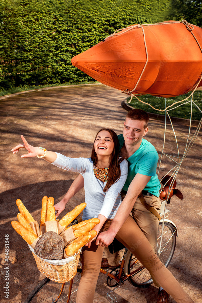 Young and joyful couple having fun in the park with bicycle and