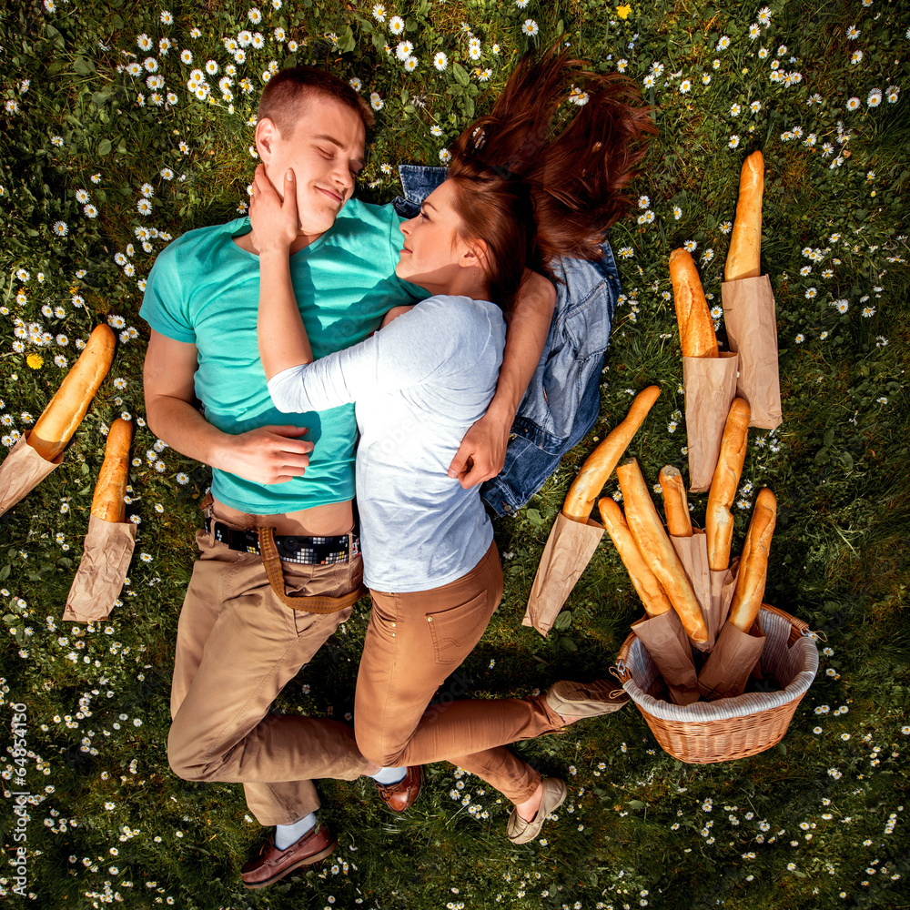 Young smiling couple lying and dreaming on the grass with basket