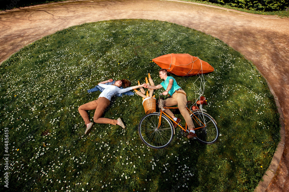 Young couple lying on the grass and riding the bicycle with red