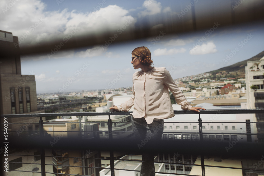 Young lady standing on a balcony with cup of coffee