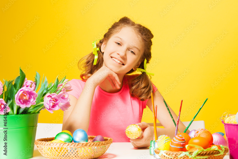 Smiling girl sits at the table with Easter eggs