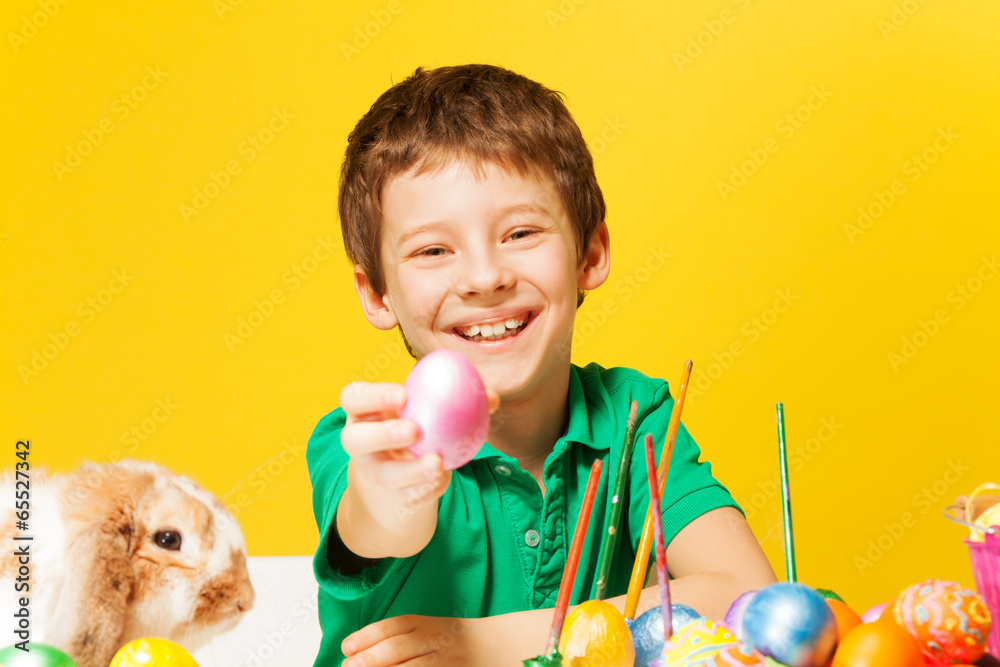 Laughing boy holds out the Easter pink egg