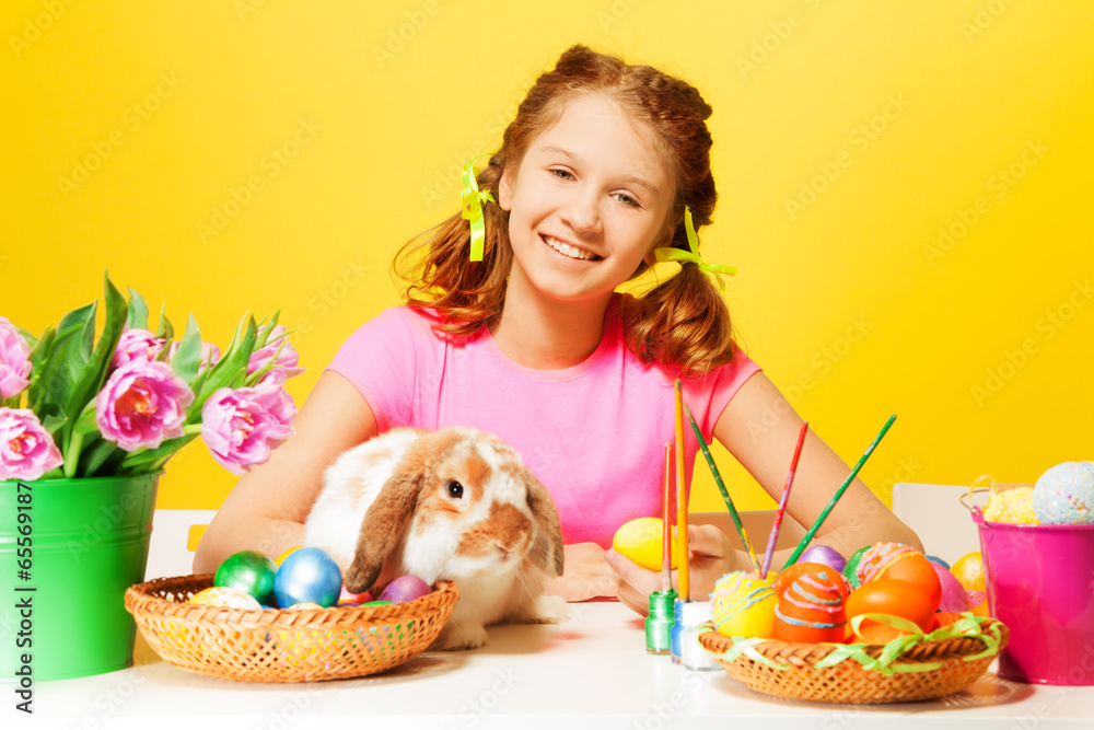 Girl sitting with Easter eggs and rabbit at table