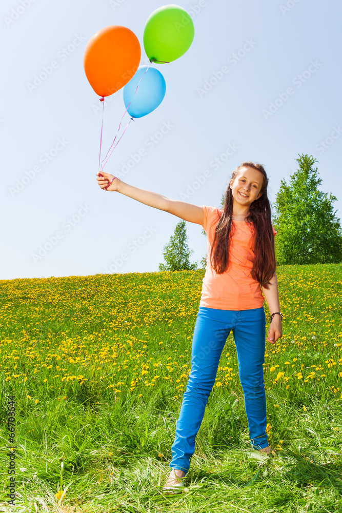 Smiling girl holding three balloons in summer