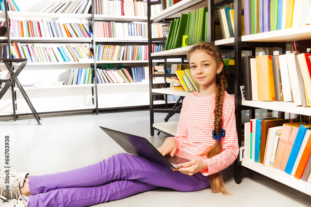 Cute girl with braid holds laptop in library