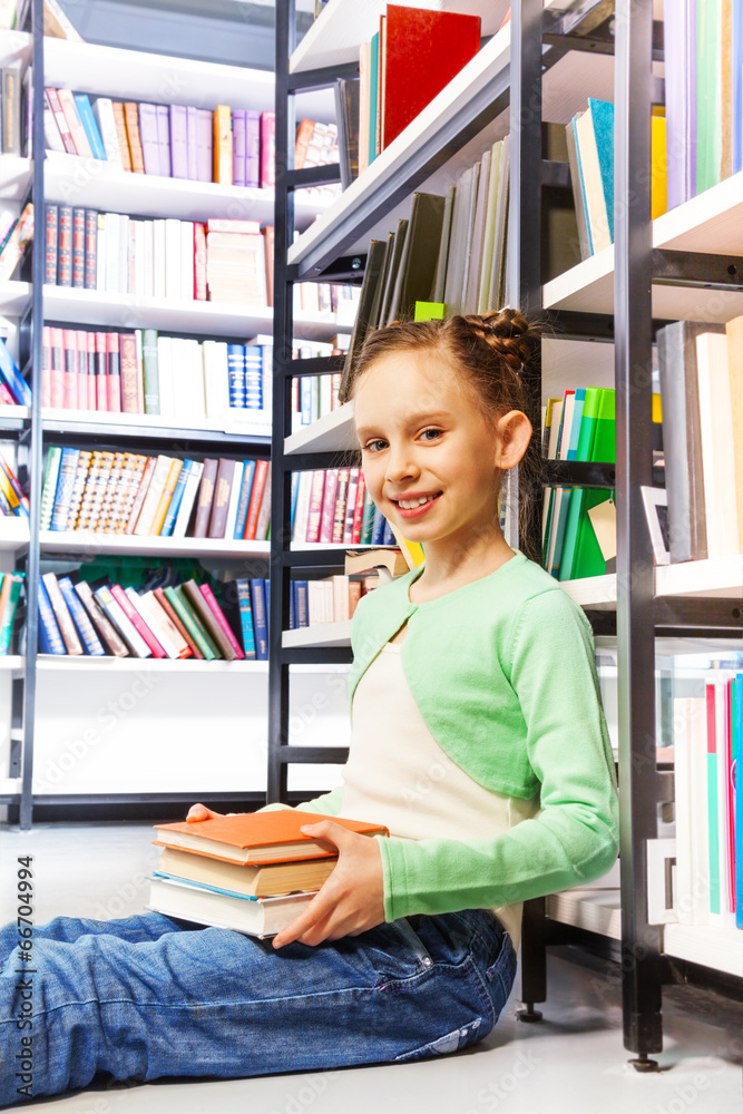 Happy girl with books sits on floor in library