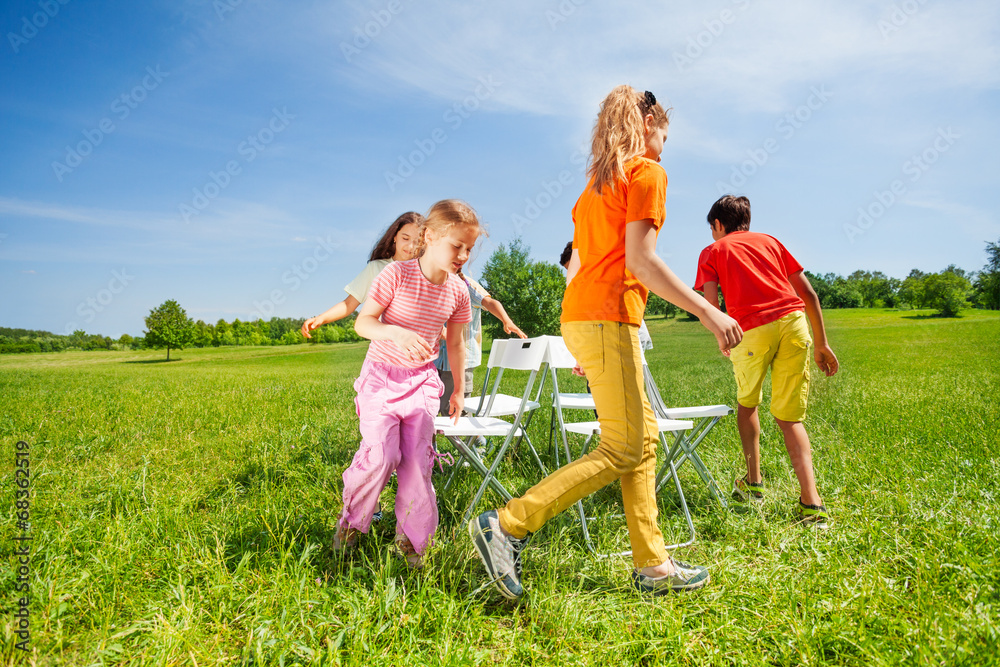 Children run around chairs playing a game outside