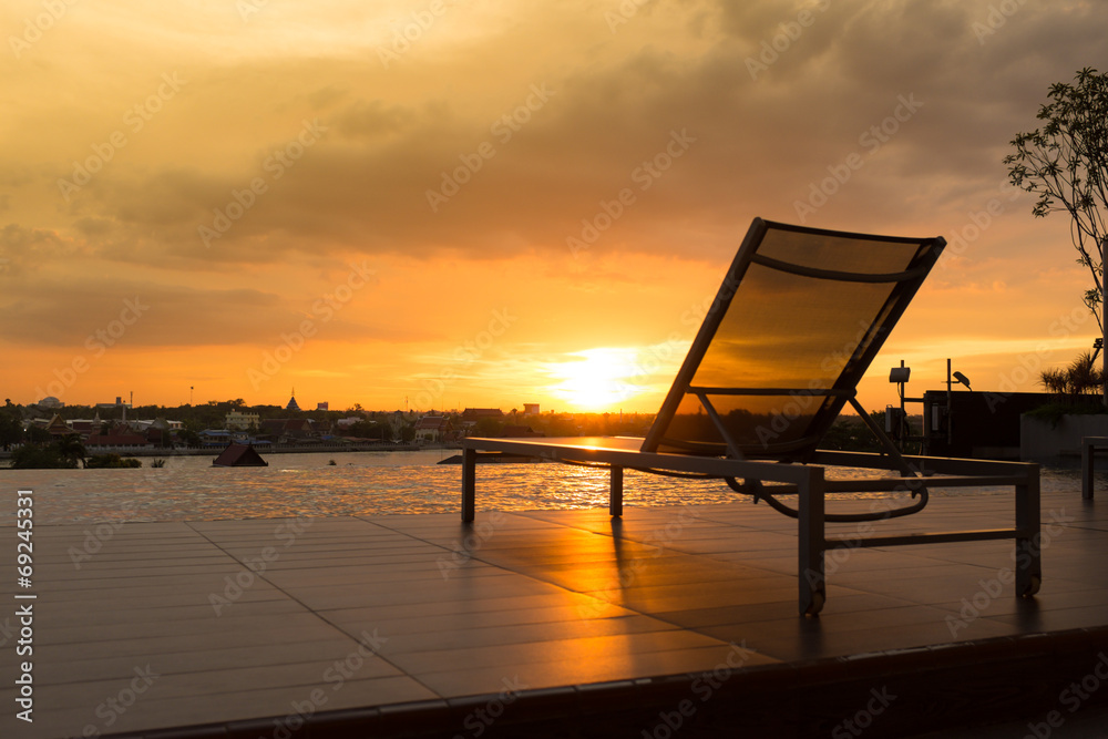 Swimming pool chair by swimming pool with sunset