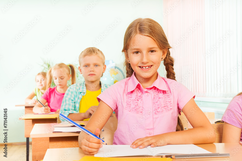 Cute girl smiles, sits at desk and writes