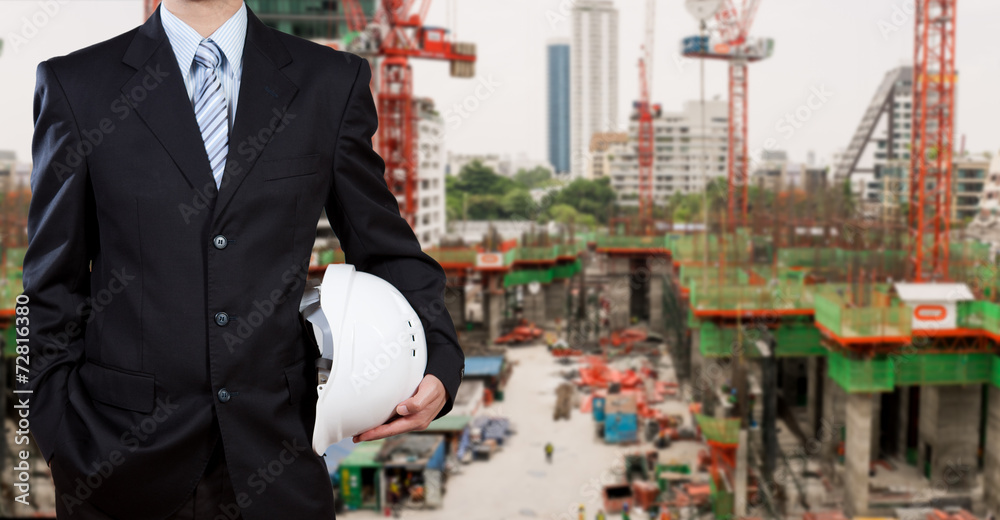 Businessman holding safety helmet with construction site in back