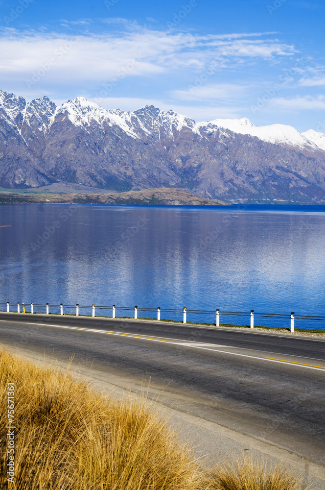 Asphalt Road With Lake And Mountain Range At The Background