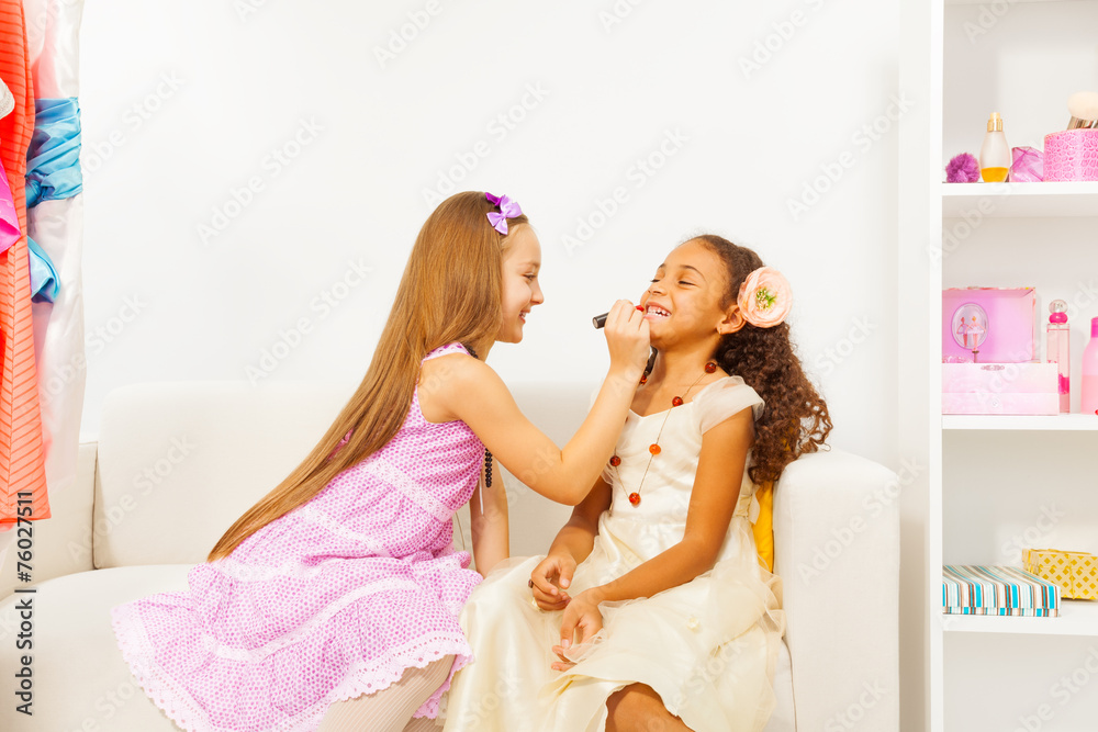 Girl with long hair applies lipstick on her friend