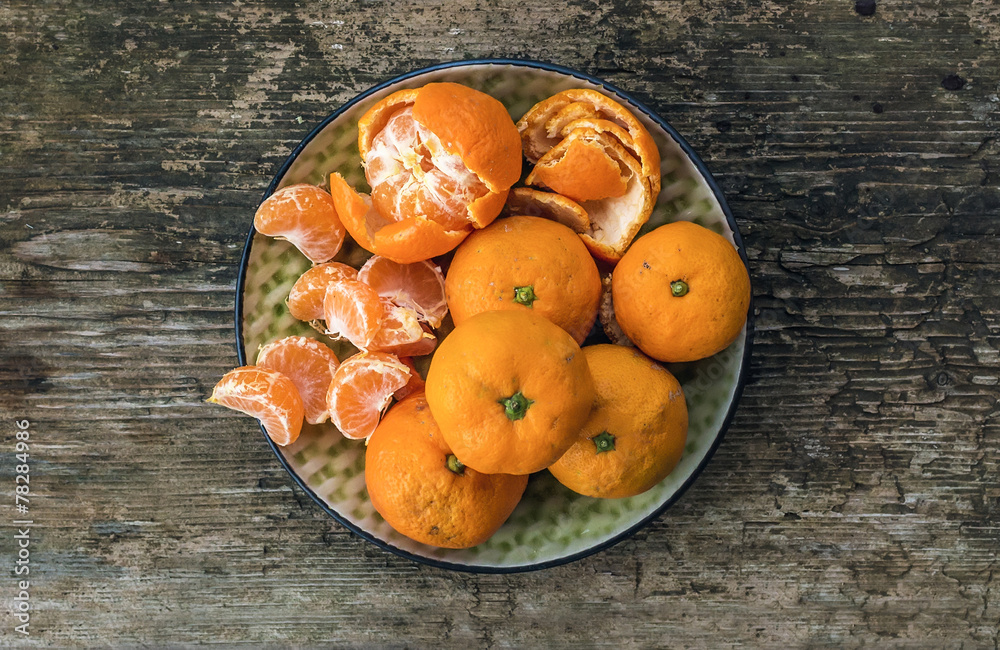 Plate of fresh ripe juicy mandarins over a rough wood background