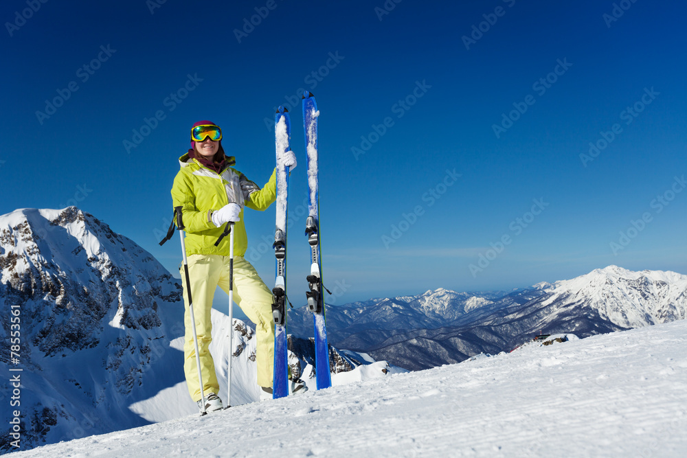 戴口罩的年轻女子站着拿着滑雪板和滑雪杆