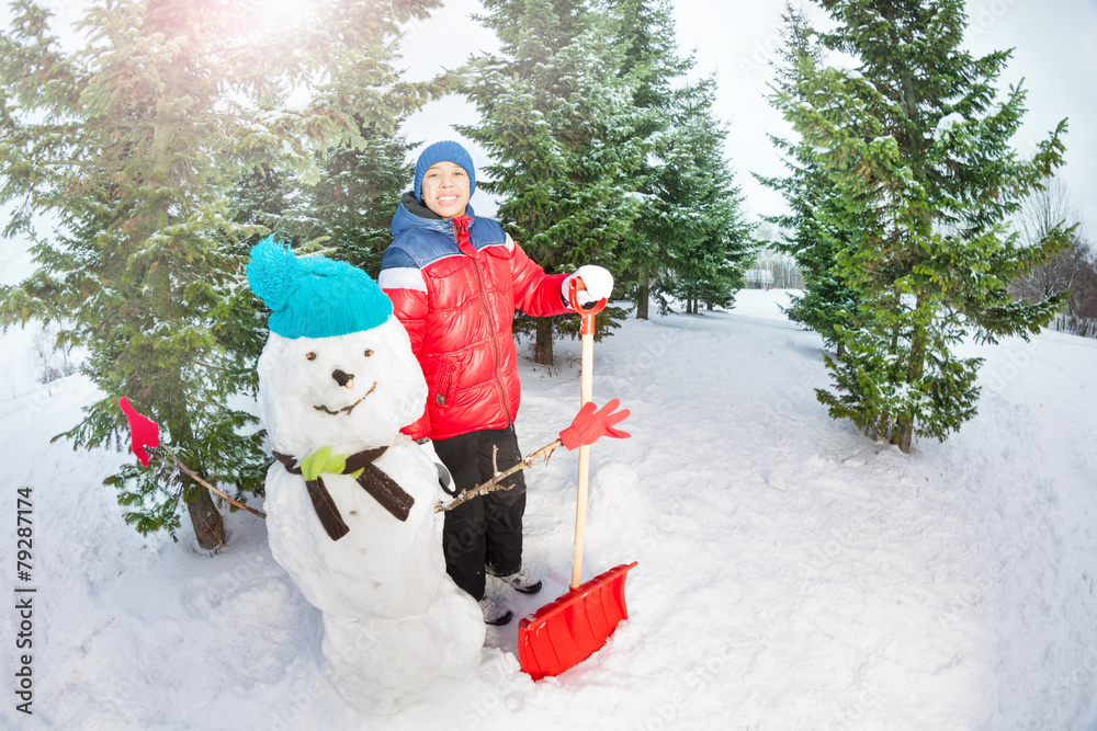 拿着铲子的阿拉伯男孩站在雪人附近