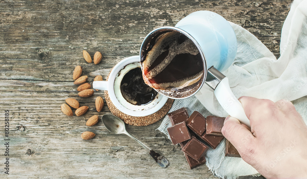 Hand pouring freshly brewed coffee from cezve - coffee pot - to