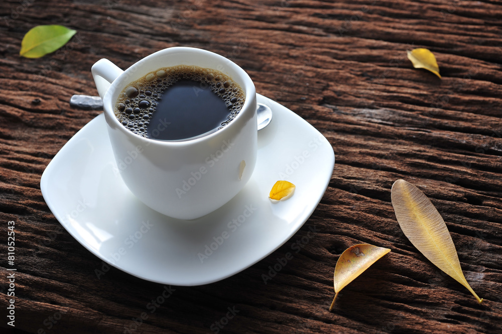 A cup of coffee on wooden table with fallen leaves