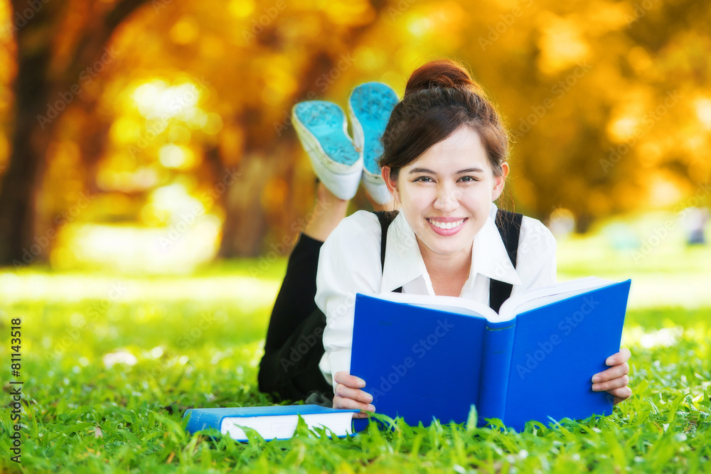 Smiling casual student lying on grass reading book