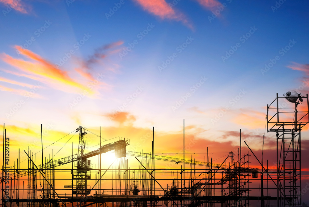 Industrial construction cranes and building silhouettes over sun