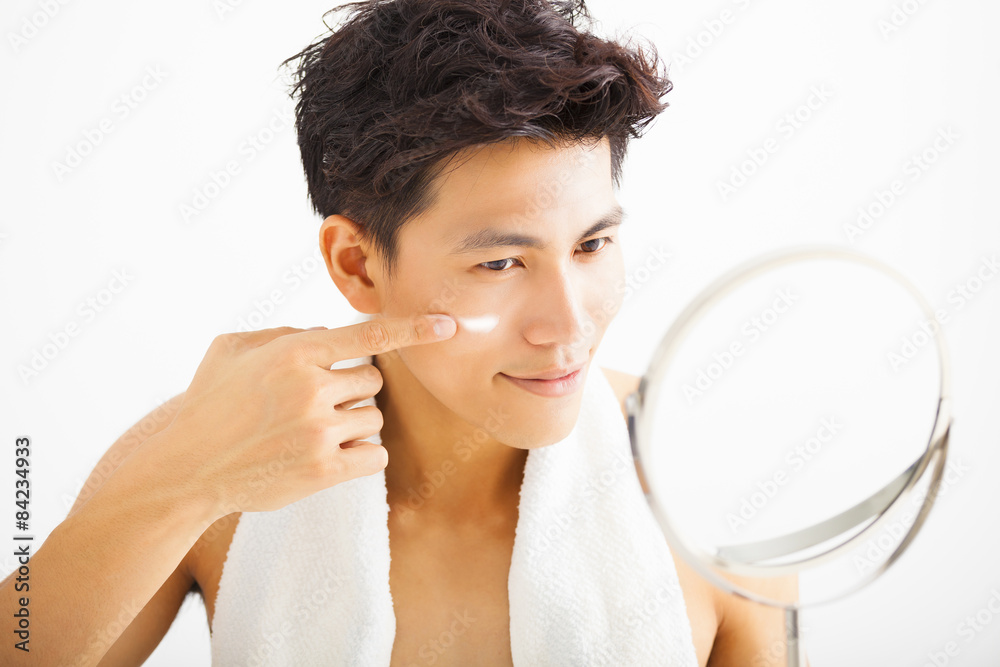 smiling man applying cream lotion on face