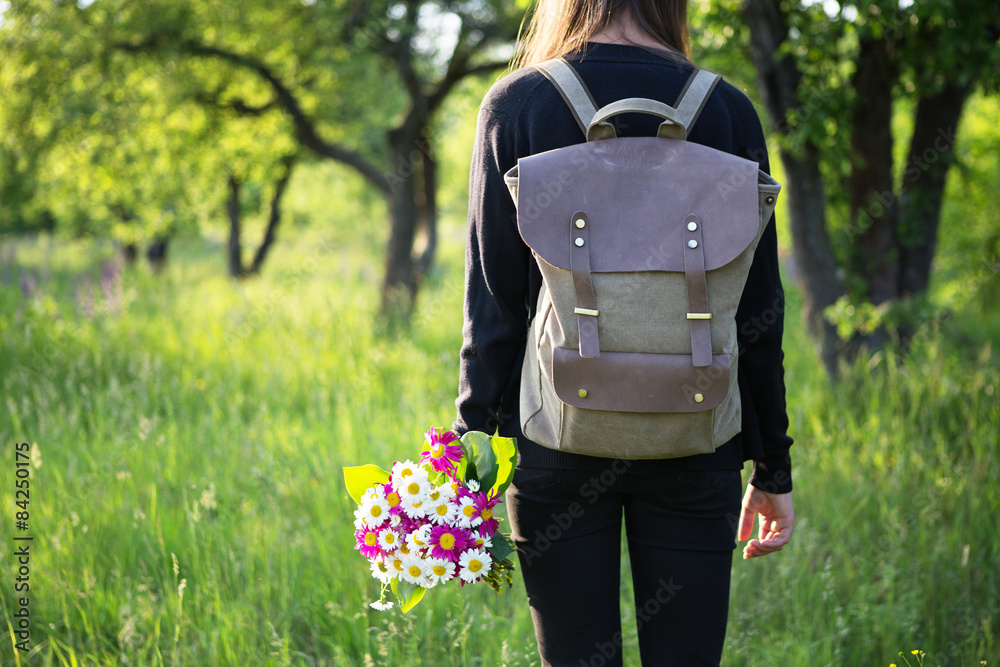 年轻女子背着背包，手里拿着鲜花徒步旅行