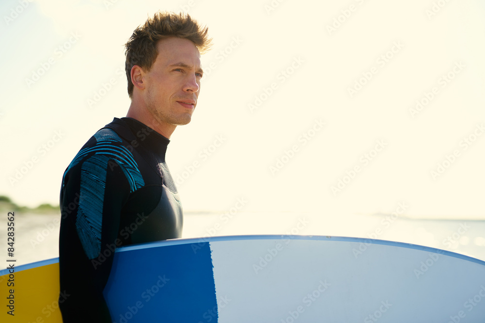 Young surfer standing on a beach at sunset