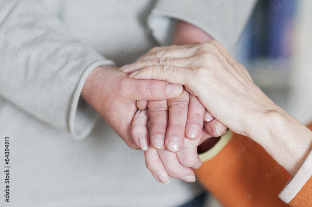 Frau haelt Hand von einer Seniorin