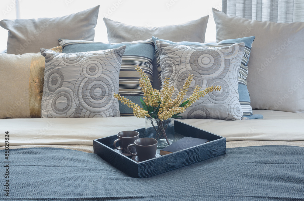 tray of cup and glass vase of plant on bed